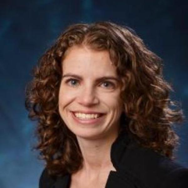 Professor with curly hair smiling posing against a blue backdrop
