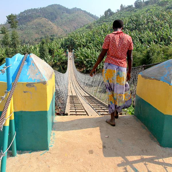a foot bridge in rwanda with a woman getting ready to cross it as seen from behind