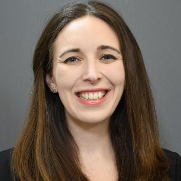 Woman with brown hair smiling in front of grey background