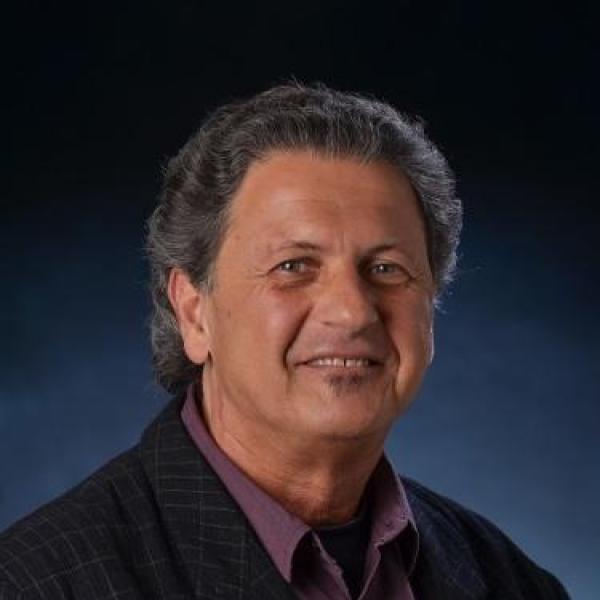 Professor with grey hair and dark colored shirt smiling