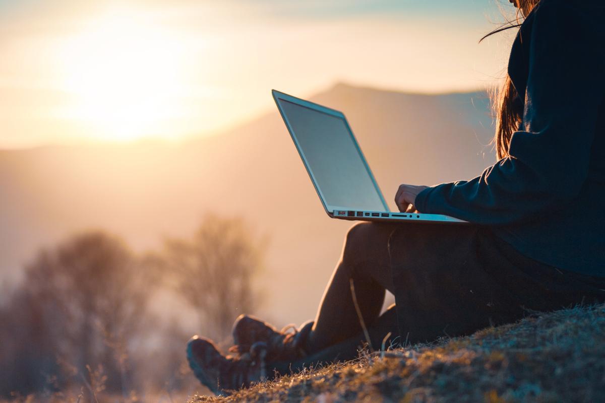 Person looking at laptop at sunrise sitting on a mountain