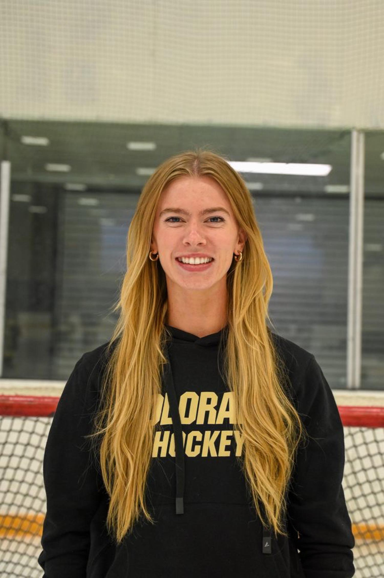 Woman with long blonde hair stands in front of hockey goal