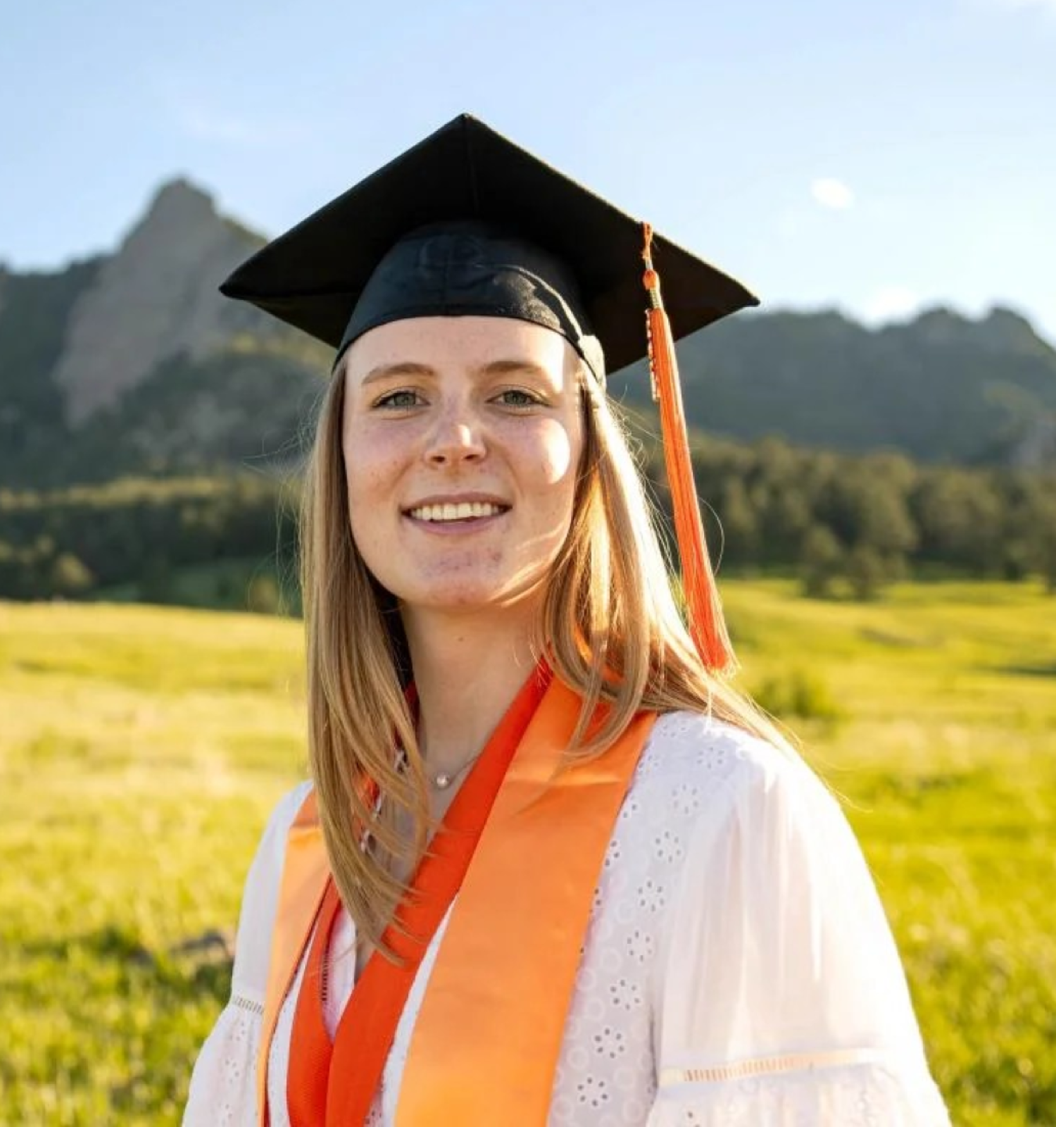 Woman in graduation cap stands in front of mountains
