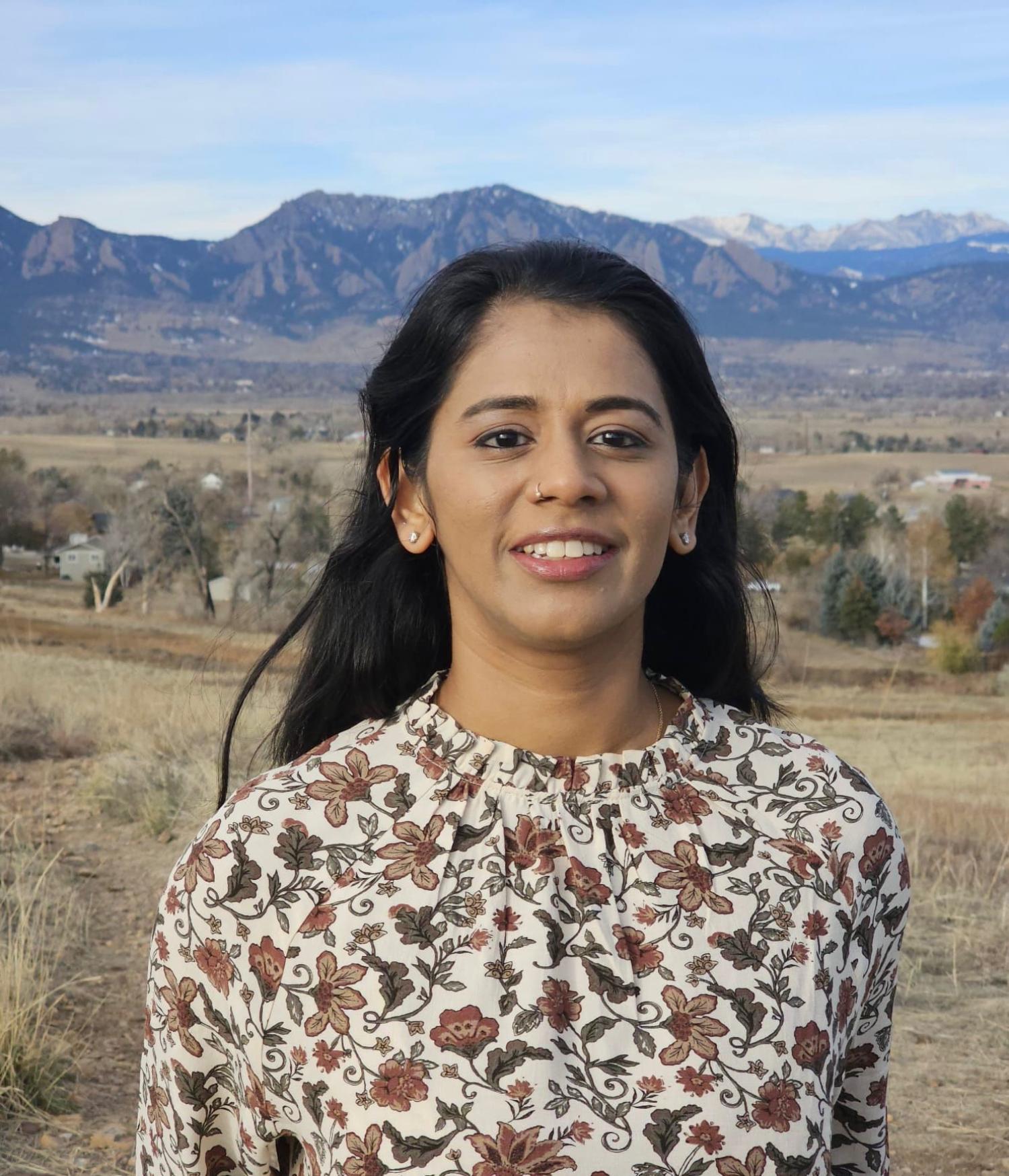 Woman in floral shirt stands in front of mountains