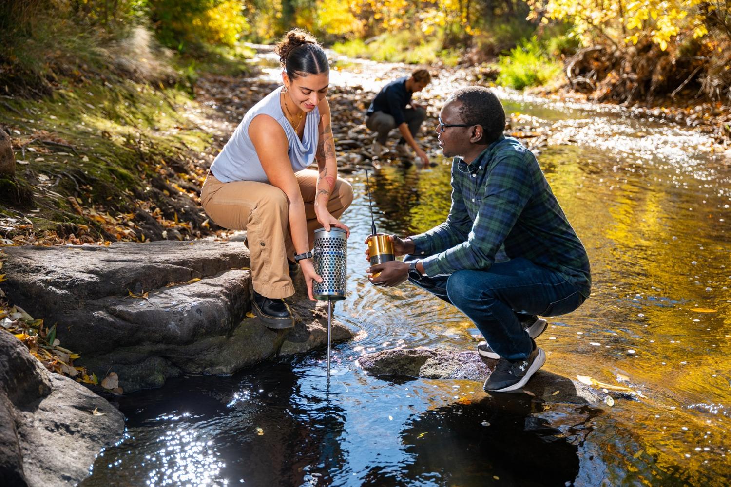 Students holding equipment by the creek on a sunny day