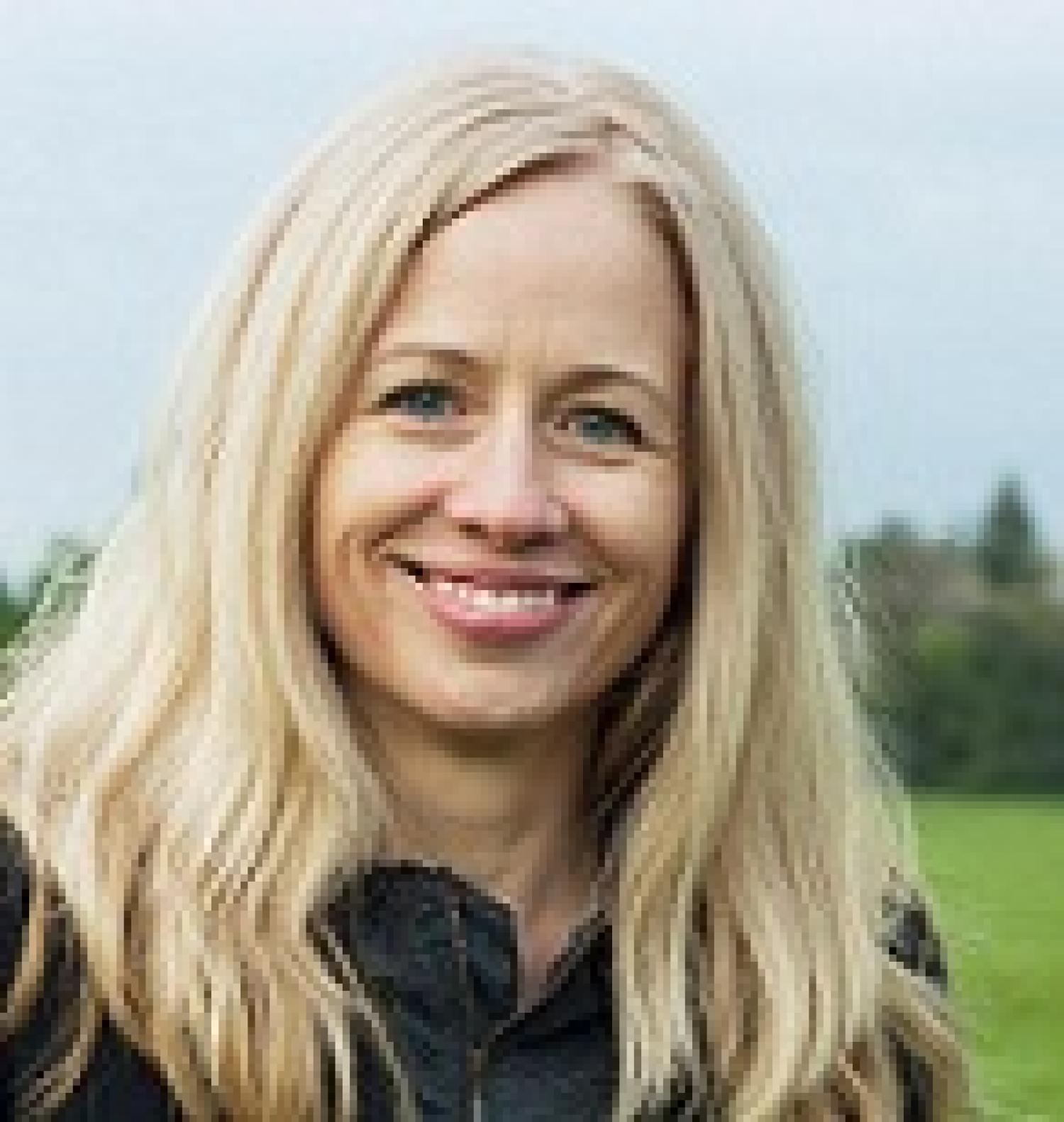 Woman smiling with blond hair, grass and trees in the background