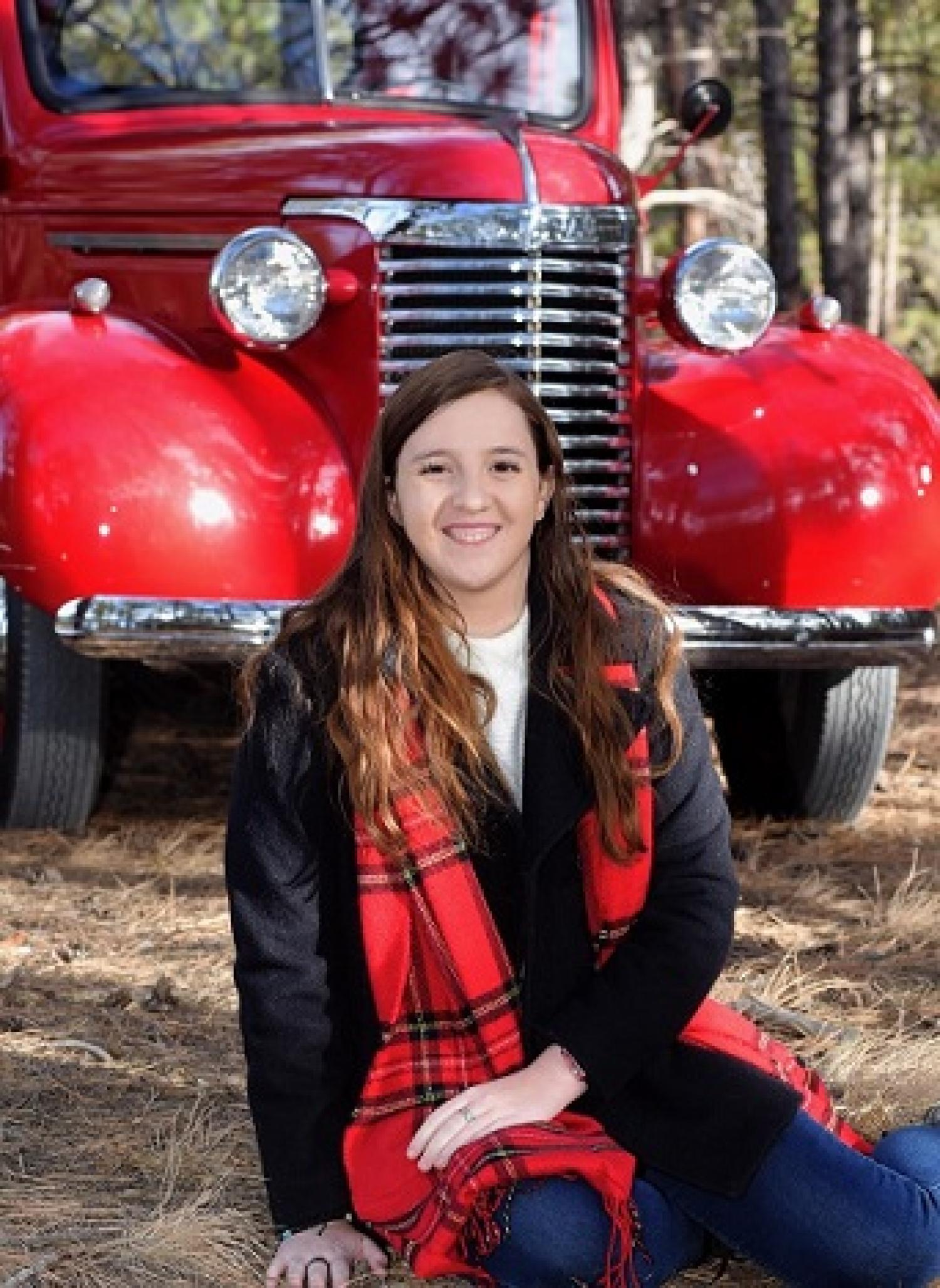 Student posed on the ground in front of a bright red classic old truck