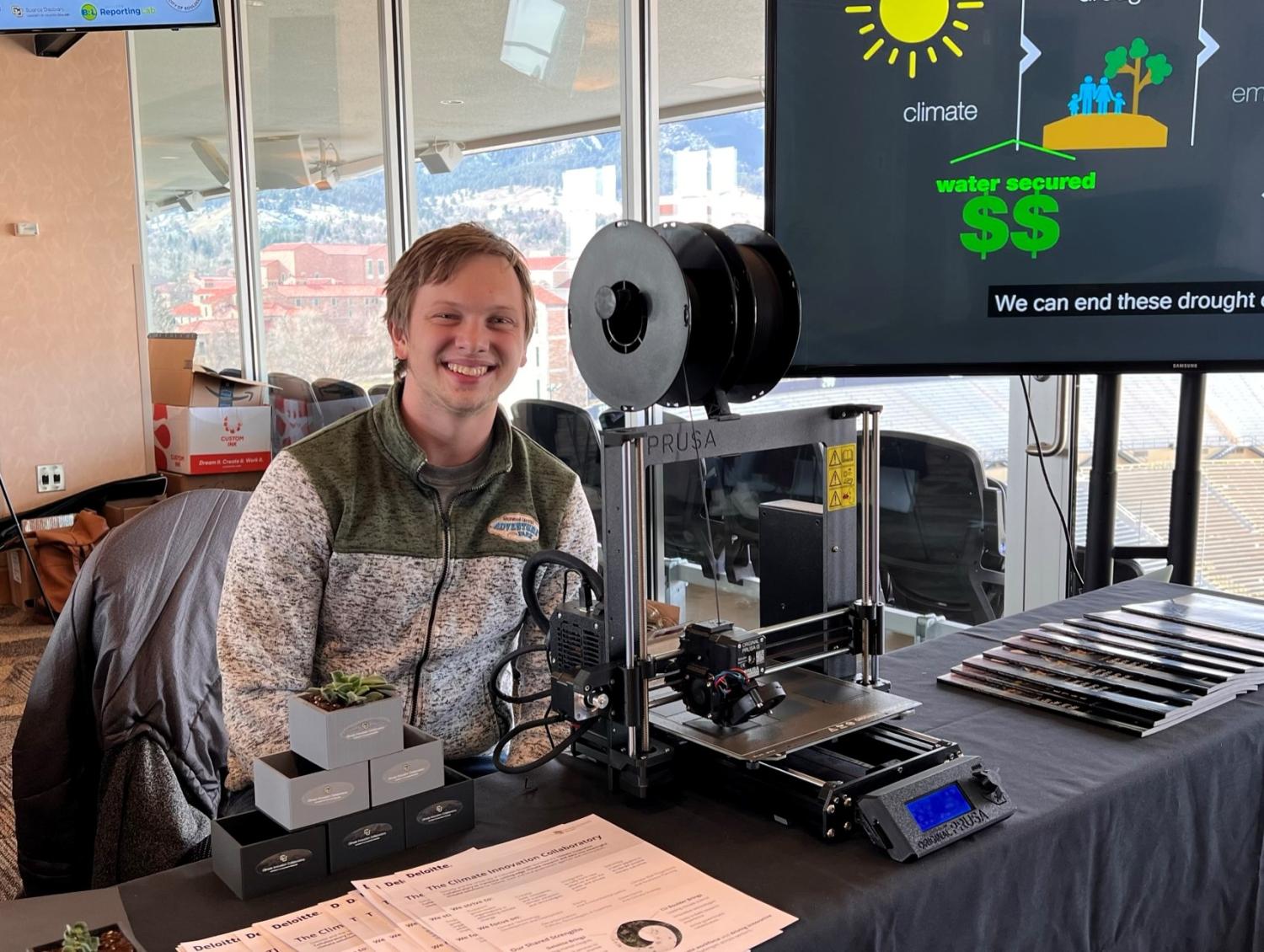 A student smiling sitting behind a 3-D printer