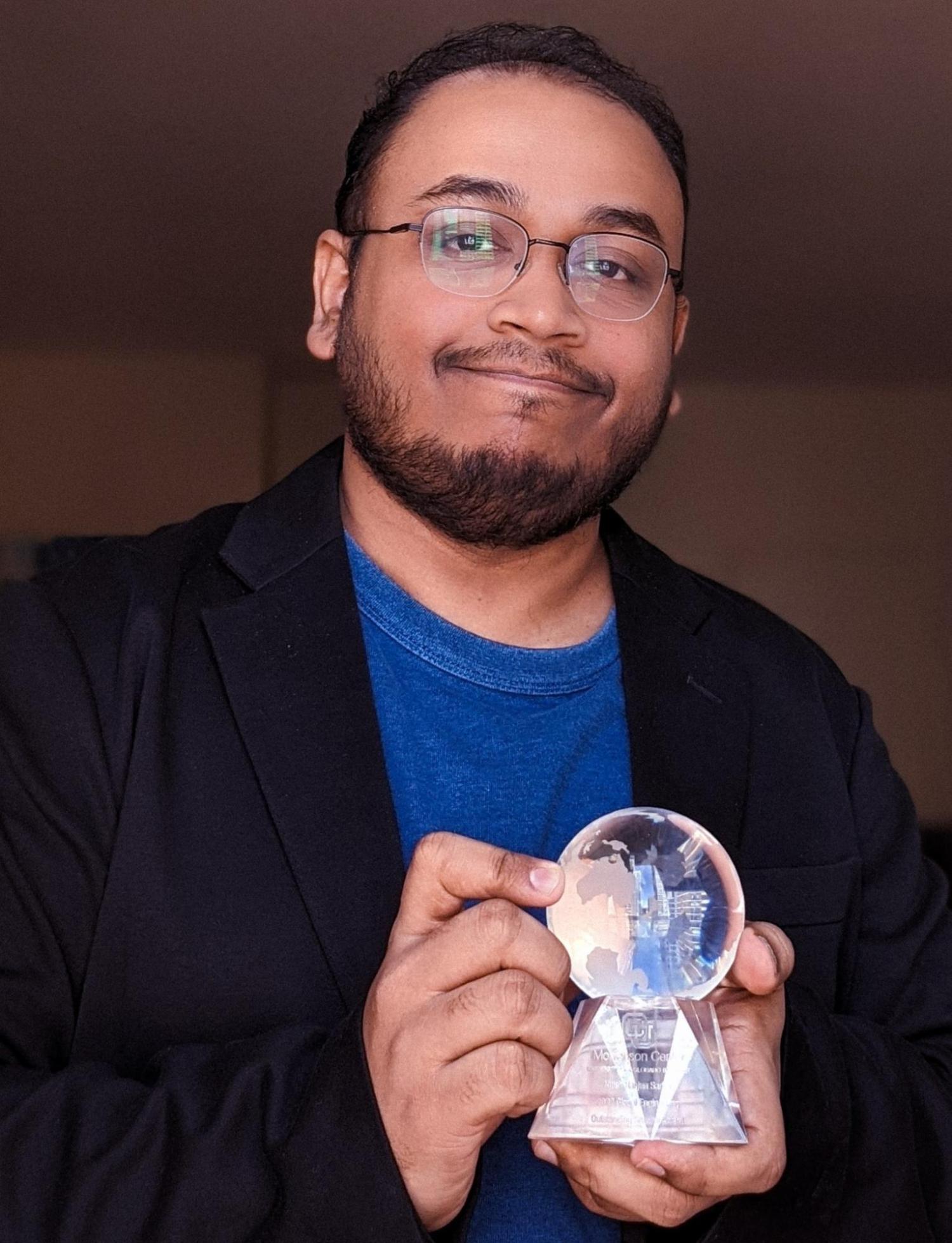 A man with a beard and glasses smiling at the camera while holding a glass globe shaped award