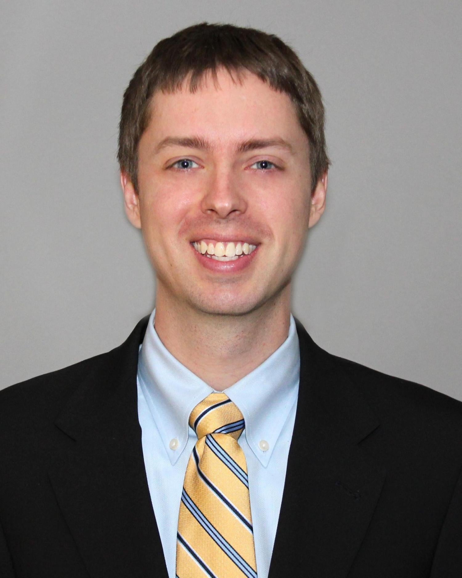 A man with short brown hair wearing a suit smiling at the camera