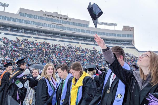 students in stadium graduating and woman throwing cap in the air