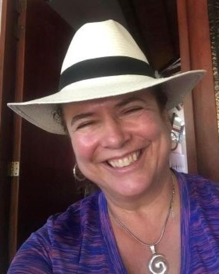 A person wearing a purple shirt and a white wide brimmed hat smiling at the camera