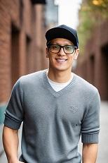 Student with glasses and a hat standing outside in front of wall
