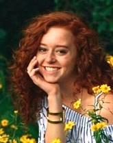 Student posing with hand on cheek against yellow flowers in an off-the-shoulder top
