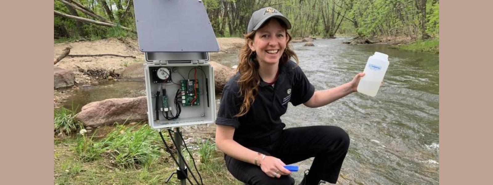 student holding water bottle up in front of creek with a piece of equipment to her side
