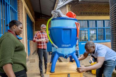 Three people gathered around and installing a water filter that is blue and plastic