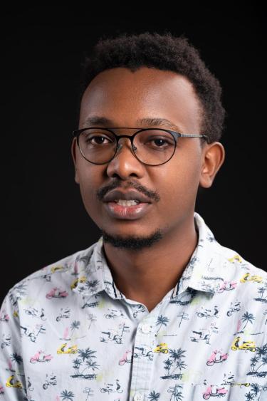 Headshot of a Student wearing black glasses and a button down shirt with pink and yellow motorcycles and palm trees on it