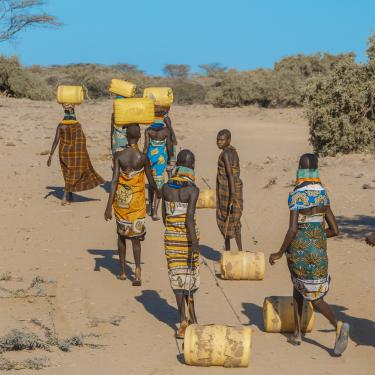 Eight people hauling water in barrels in dry area of Kenya