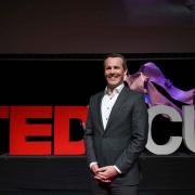 man in suit standing in front of red TEDxCU sign