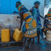 three women filling up yellow jerry cans at an outdoor tap