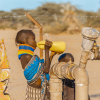 child in traditional African clothing drinking water from a yellow jerry can