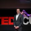 man in suit standing in front of red TEDxCU sign