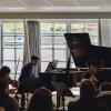 A piano trio performing in front of a large window