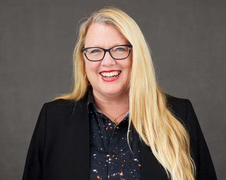 Photo of Barbra, blond hair, glasses, black jacket