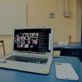 A computer sits on a desk with a Zoom meeting on the screen