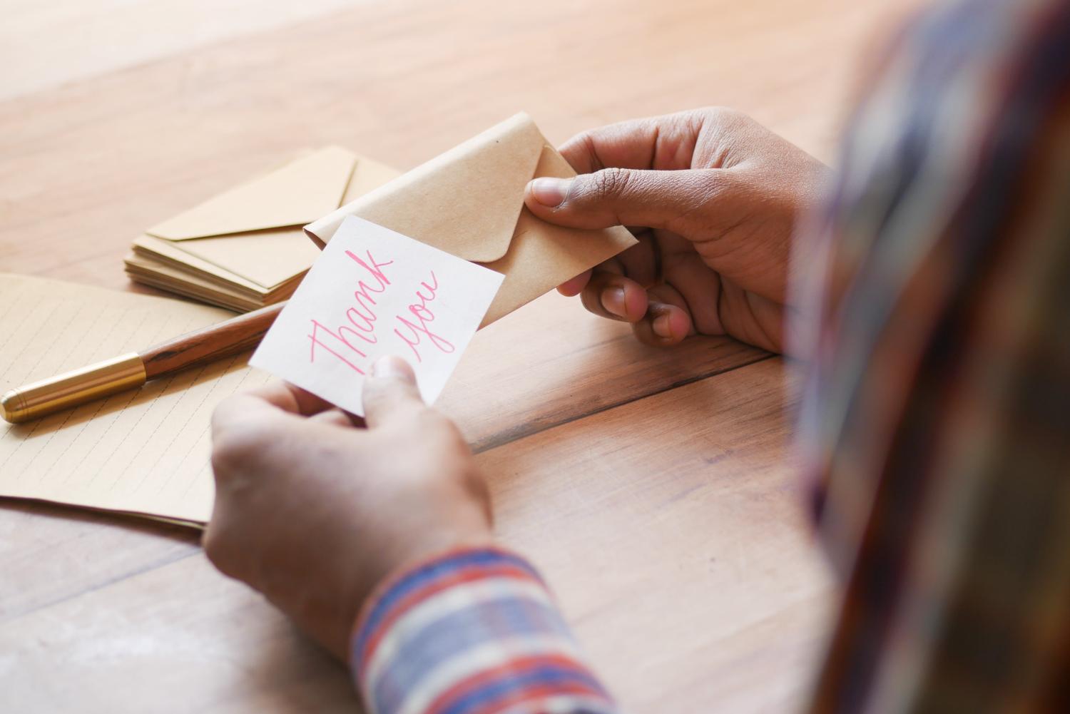 A person opens an envelope and pulls out a thank you card