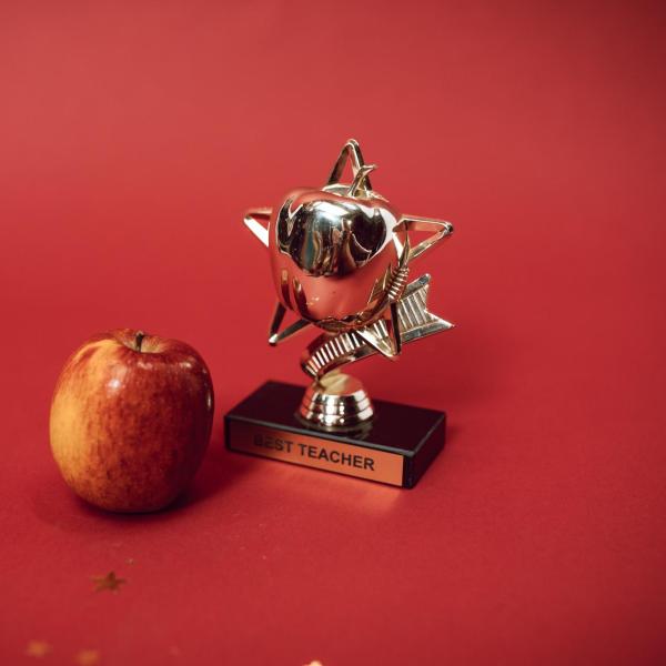 an award trophy for best teacher on a red table next to a red apple