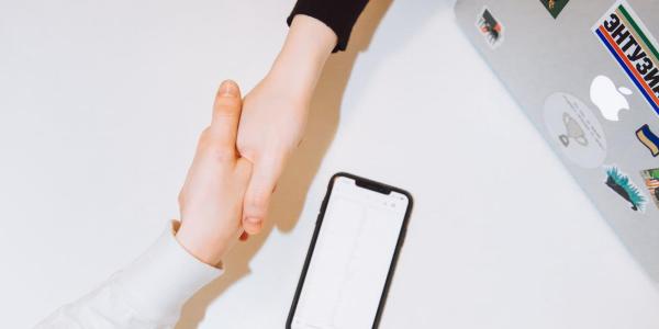 two hands shaking with pencil and paper on a table beneath them