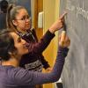 Two students work a chemistry problem at a blackboard