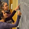 Two students work a chemistry problem at a blackboard