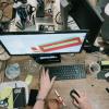 Hands work at a computer sitting on a crowded desk