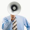 person in a blue button up shirt with a tie holds a megaphone in front of their face