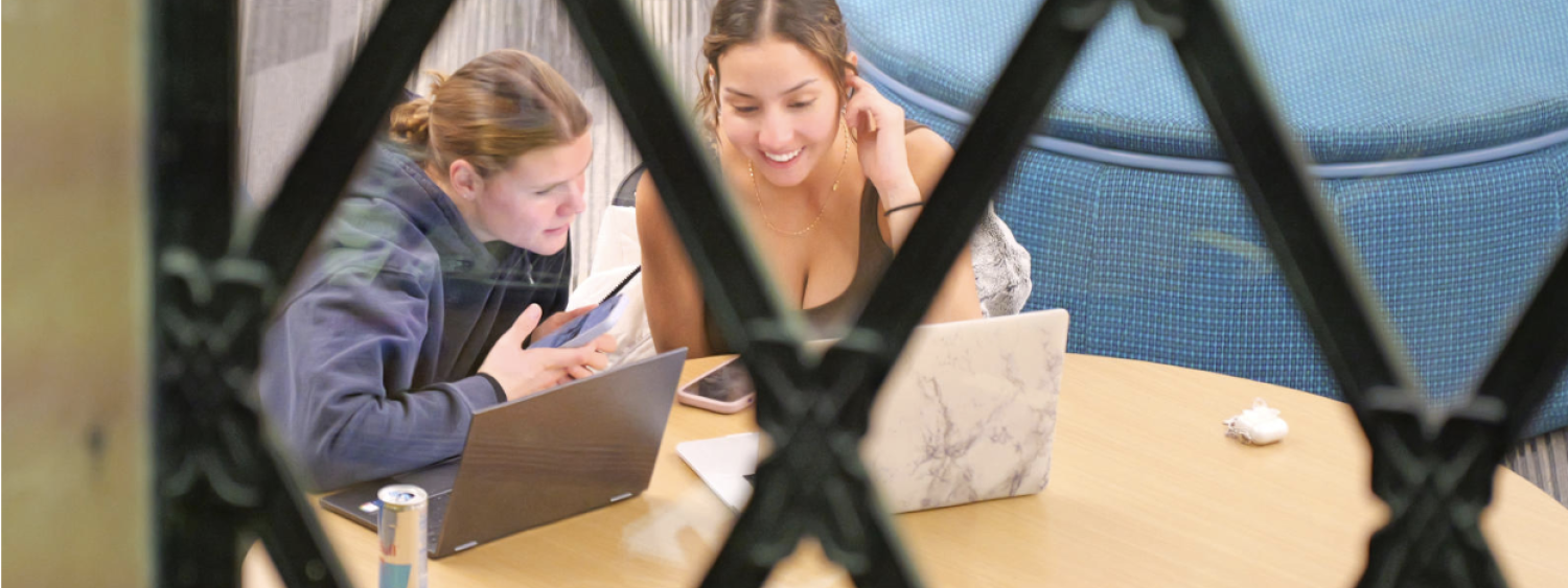 Two students work together on homework with a laptop at a table