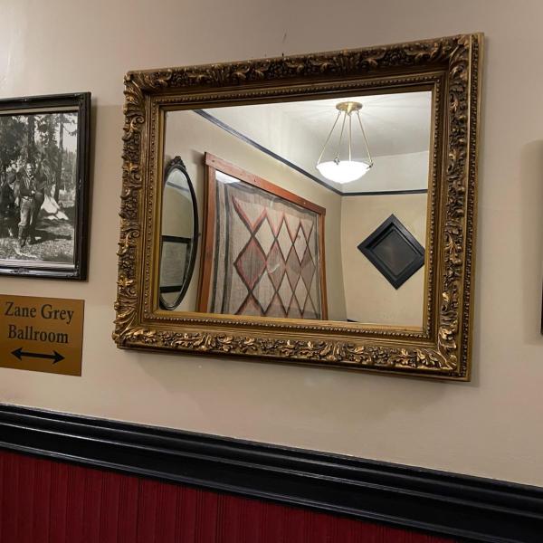 A sign for the Zane Grey Ballroom at the Weatherford Hotel hangs with a photo of Zane Grey surrounded by various mirrors and interior design elements.