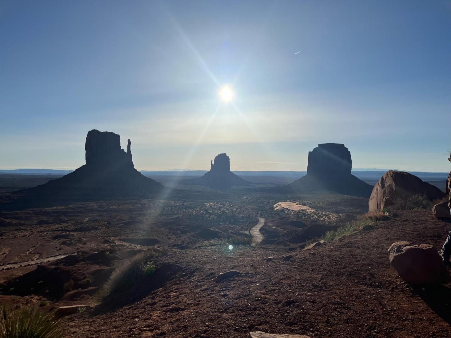 Iconic view of West Mitten Butte, Merrick Butte, and East Mitten Butte at Monument Valley Navajo Tribal Park with morning sun overhead.