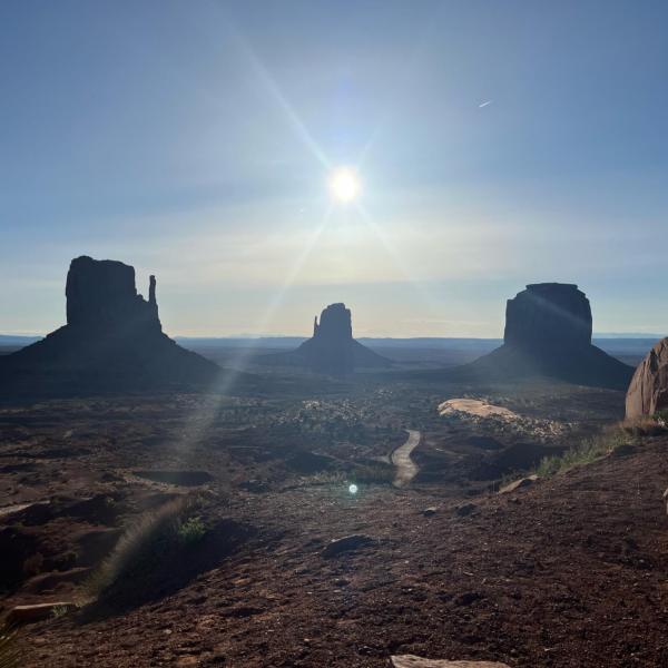Iconic view of West Mitten Butte, Merrick Butte, and East Mitten Butte at Monument Valley Navajo Tribal Park with morning sun overhead.