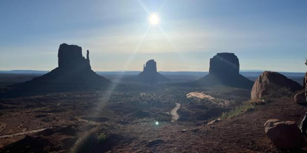 Iconic view of West Mitten Butte, Merrick Butte, and East Mitten Butte at Monument Valley Navajo Tribal Park with morning sun overhead.