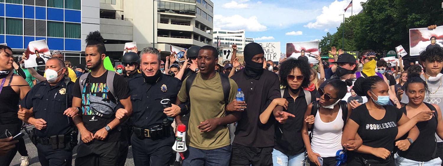 photo of people interlocking arms with a police officer at the Black Lives Matter protests
