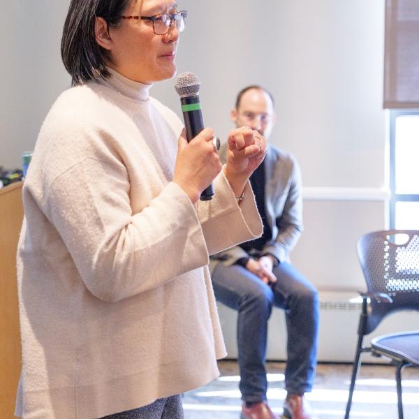 Jennifer Ho holding a microphone, with Caleb Elfenbein shown in background