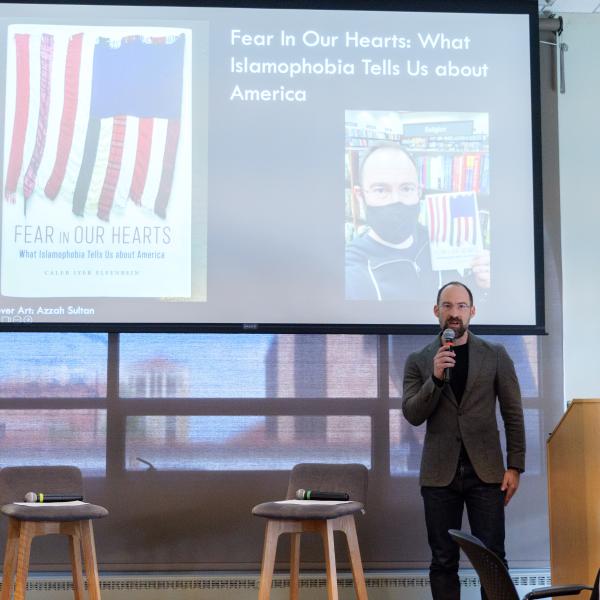 Caleb Elfenbein presenting his work with his powerpoint behind him that highlights his book