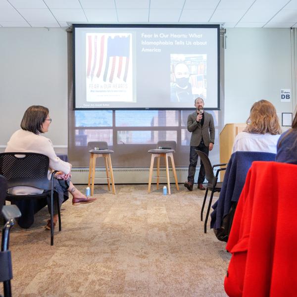 Caleb Elfenbein presenting his work with his powerpoint behind him; audience is shown