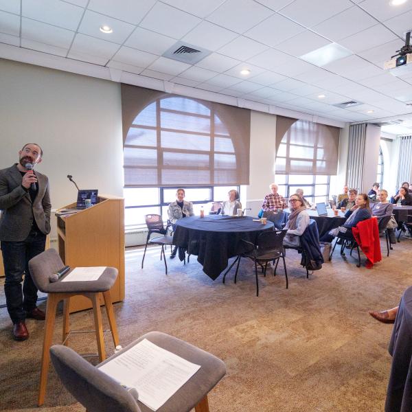 Caleb Elfenbein at podium with audience featured