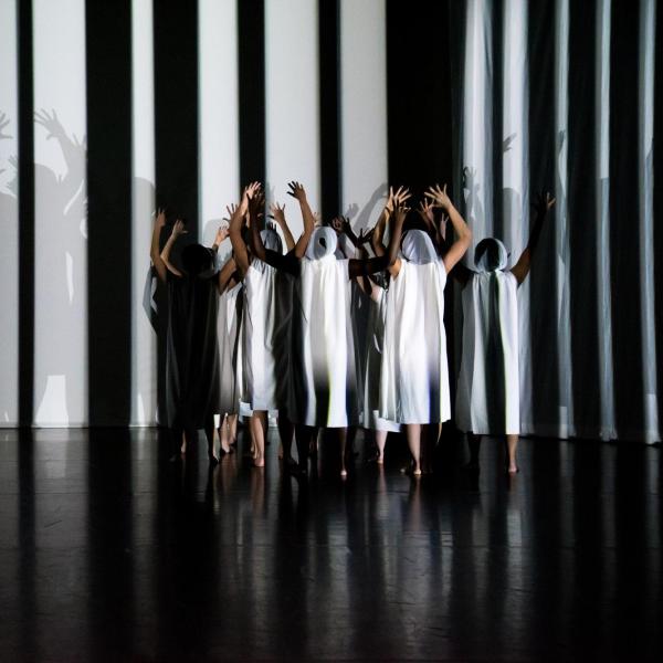 Dancers wearing black and white clothing with their arms raised on a stage