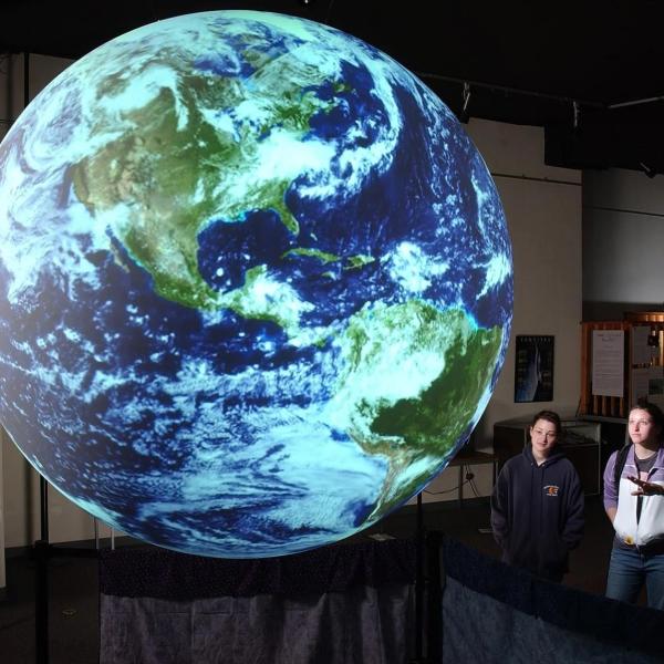 A virtual image of planet Earth with three figures looking at it