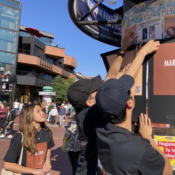 Participants hang posters on a space outside. The posters have dates with the hashtag "stop asian hate". Date visible is March 3, 1885.