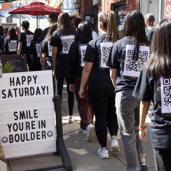 Group of people from political art performance is seen wearing a black shirt; back shown is a QR Code. The QR code, if scanned, corresponds to landmark civil rights case.